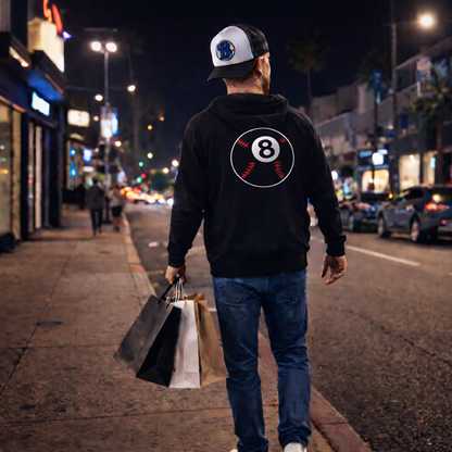 Man walking on a city street at night with shopping bags, wearing a hoodie with a logo.