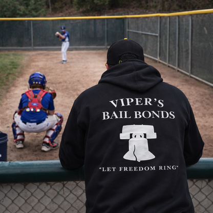 Person wearing a black hoodie with 'Viper's Bail Bonds' text and graphic at a baseball game.